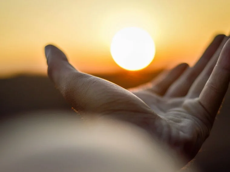Une main ouverte tendue vers le soleil couchant
